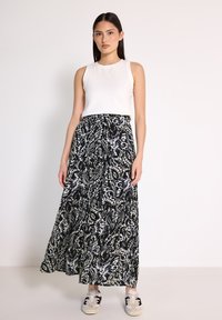 Bílý bezrukávový top v kombinaci s dlouhou černou sukní s paisley vzorem v modré a bílé barvě. Modelka má na sobě tenisky.