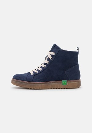 Granatowy zamszowy wysoki sneaker z beżowymi sznurowadłami, brązową gumową podeszwą i małą zieloną metką z logo po stronie, pokazany z profilu.