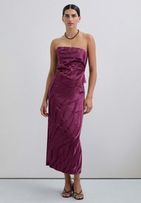 Vestido burdeos sin mangas con un brillo texturizado, que presenta un corpiño ajustado, una falda acampanada y sutiles patrones en forma de olas, acompañado de sandalias negras.