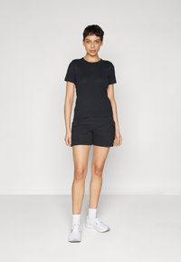 Sort bomulds t-shirt kombineret med sorte cargo shorts med sidelommer. Modellen har hvide sportssko med ankelstrømper på. Enkel, tætsiddende design.