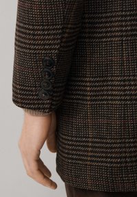 Blazer de cuadro de lija marrón con una mezcla de lana texturizada, cuatro botones negros y un corte ajustado en las mangas.