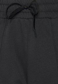 Černé tepláky z měkké látky s elastickým pasem a černým šňůrkovým stahováním. Mají boční kapsy a hladký povrch.