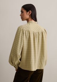 Grüne karierte Bluse mit luftigen Ärmeln, Kragen und gerafftem Rückendetail. Hergestellt aus weichem Stoff mit leichtem Textur.