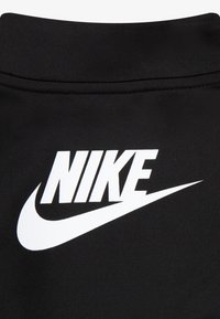 Material negru pentru îmbrăcăminte sportivă cu un logo alb proeminent „NIKE” și o swoosh. Designul este curat și simplu, sporind vizibilitatea brandului.