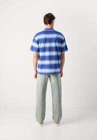 Camisa de manga corta en tonos azules con rayas horizontales. Tejido suave, corte relajado, combinada con unos jeans sueltos de color azul claro.
