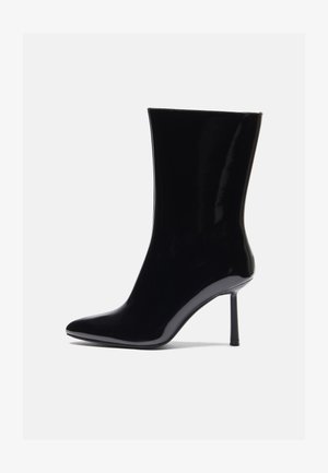Musta patenttivati nahkasaapas, jossa on terävä kärki ja hoikka stiletto-korko, jonka pinnassa on sileä, kiiltävä pinta ja minimalistinen muotoilu.