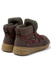Zapatillas de media caña marrones con tejido texturizado, cuello acolchado, cordones rojos y una suela de goma flexible y moteada con un parche de logo.