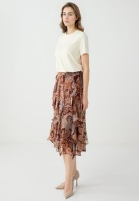 Beige top met korte mouwen gecombineerd met een bruine rok met een patroon en gelaagde ruffles. Draag het met lichtbeige hoge hakken.