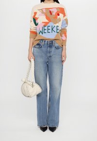 Sweter na drutach z wielokolorowymi kwiatowymi wzorami i napisem „WEEKEND”, zestawiony z jasnoniebieskimi szerokimi spodniami jeansowymi oraz białą plecioną torebką.