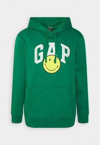 Sudadera verde con capucha, hecha de mezcla de algodón, con texto blanco "GAP" y un gráfico de cara sonriente amarilla. Bolsillo canguro delantero y capucha ajustable.