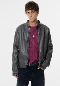 Mænds grå faux læderjakke med opretstående krave, frontlynlås og to sidelommer, båret over en tekstureret lilla sweater.
