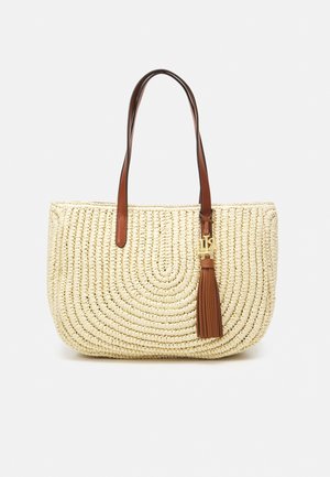Beżowa pleciona torba typu tote z brązowymi skórzanymi uchwytami oraz pasującym skórzanym brelokiem z chwostem i złotym akcentem.