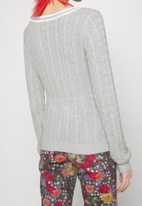 Ljusgrå ribbad tröja med kabelstickad textur, långa ärmar och vit accent längs halsringningen, i kombination med blommönstrade byxor.