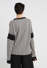 Randig tröja med en blandning av ljus och mörk grå toner, med breda och smala mönster, långa ärmar och svarta ribbade detaljer.