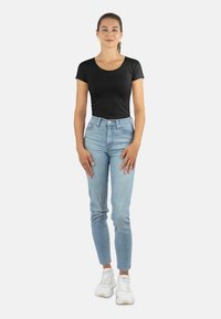 Schwarzes, kurzärmeliges, tailliertes Oberteil, hellblaue, hochgeschnittene Jeans, weiße Sneaker, lässiger Look, glattes Material und schmal zulaufendes Bein.