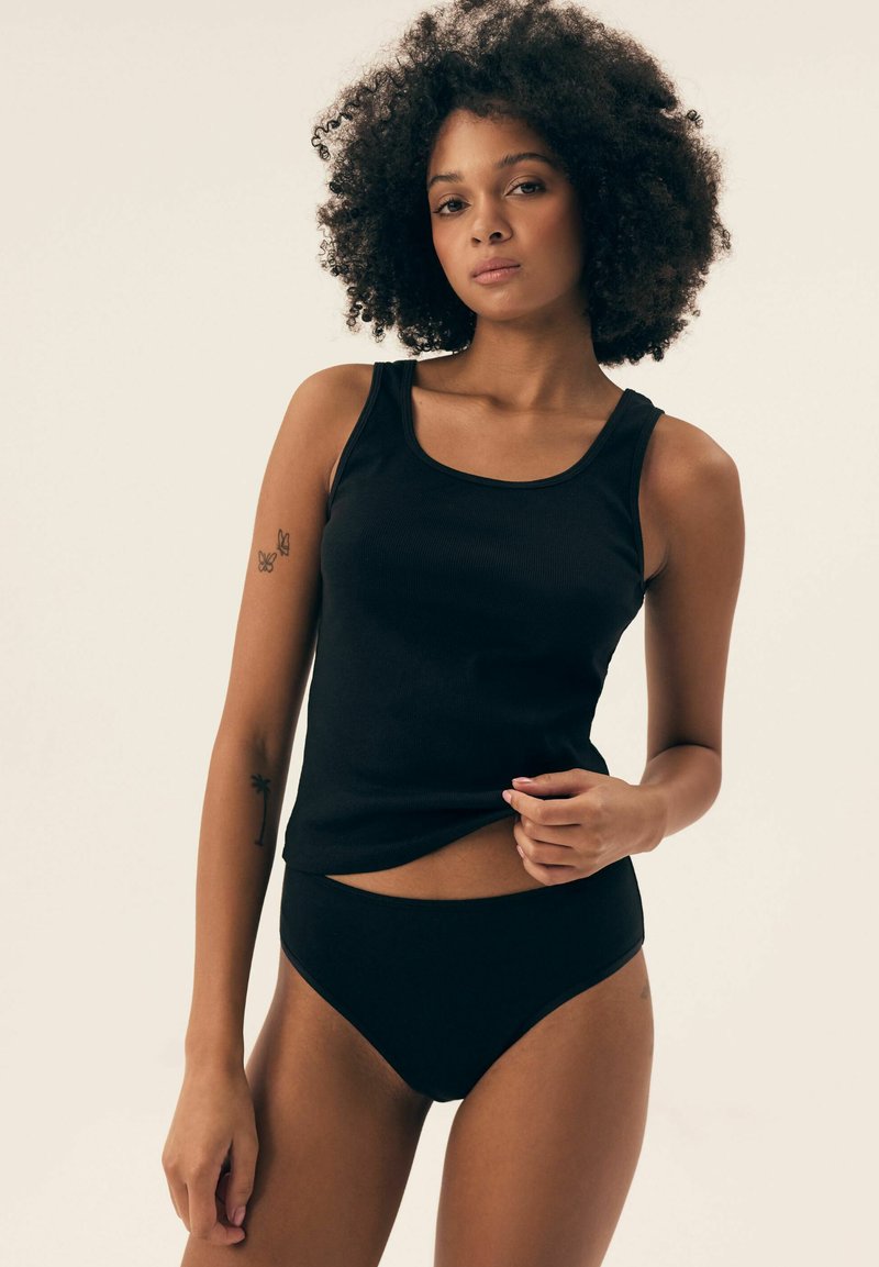 Czarny prążkowany top na ramiączkach z szerokimi paskami, w połączeniu z czarną bielizną o wysokim stanie. Gładki materiał, dopasowany krój, minimalistyczny styl.