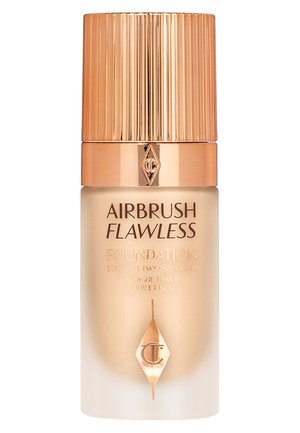 Fond de teint Airbrush Flawless dans un flacon transparent haut avec un bouchon doré strié ; comporte des marques et des revendications imprimées en texte doré.