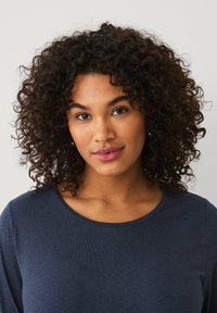 Marineblauw langärmelig shirt met een ronde hals. De stof lijkt zacht met een gladde textuur. Het model heeft krullend haar en een neutrale achtergrond.