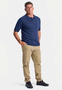 Tmavě modré polo tričko s krátkými rukávy a plochým límečkem, v kombinaci s béžovými chino kalhotami a černými teniskami, vytváří ležérní a čistý vzhled.