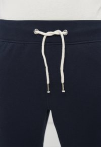 Gros plan d’un pantalon de survêtement bleu marine avec un cordon blanc noué en un nœud simple à la taille élastique.