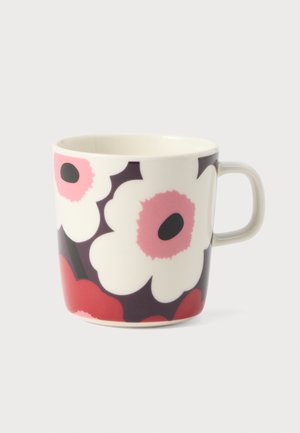 Mug en céramique blanche avec des motifs de fleurs roses et rouges aux centres noirs, présentant une anse simple sur un fond gris clair.