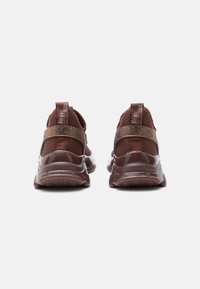Un paio di sneaker marroni con tessuto a rete, cinturini glitterati e linguette del tallone con marchio, viste da dietro su uno sfondo bianco.
