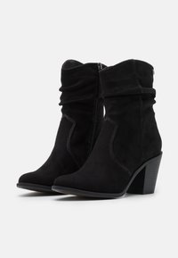 Czarne zamszowe botki za kostkę z luźnym cholewką, spiczastym noskiem i grubym obcasem, z kontrastowym przeszyciem i bocznym zamkiem błyskawicznym.
