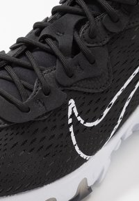 Baskets noires en tissu texturé, lacets noirs passés dans des œillets, logo Nike swoosh blanc et semelle blanche avec motif antidérapant.