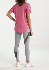 Top rosa a maniche corte con maniche arrotolate abbinato a leggings grigi con motivi geometrici in verde oliva e scarpe da ginnastica bianche.
