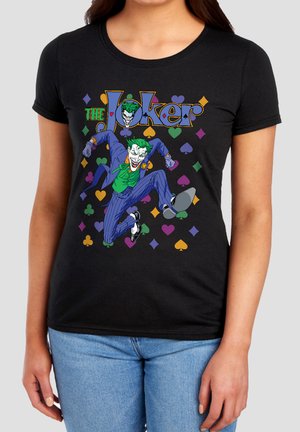 Woman wearing a black t-shirt with a colorful Joker graphic jumping, surrounded by multicolored playing card suit symbols and the text "The Joker".