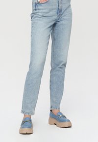 Niebieskie loafersy z masywną beżową podeszwą, z ozdobami w kolorze złota, zestawione z jasnoniebieskimi dżinsami o prostym kroju, z kieszeniami.