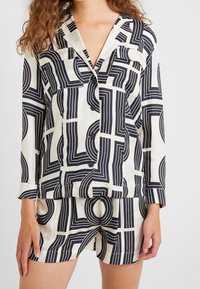 Ensemble de pyjama à manches courtes noir et blanc à motifs, présentant des lignes géométriques et des cercles, fabriqué dans un tissu lisse avec des boutons sur la chemise.