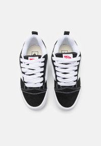 Paire de baskets Vans noires et blanches avec lacets blancs, coutures visibles et logo rouge Vans sur la languette, vues de dessus.