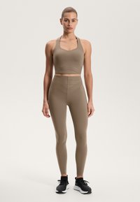 Hnedá súprava športového oblečenia pozostávajúca z priliehavého športového podprsenky s výstrihom do štvorca a legín s vysokým pásom, oboje z hladkého a elastického materiálu.