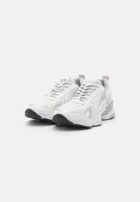 Scarpe sportive bianche con pannelli in rete e sintetici, suole testurizzate e accenti grigio chiaro. Presentano una punta arrotondata, lacci e marchio.