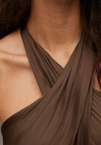 Vestido marrón sin mangas con tela drapeada, que presenta un diseño cruzado en el escote y una textura suave y fluida.