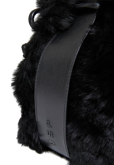 Borsa in finta pelliccia nera con una tracolla in pelle nera opaca e liscia, decorata con testo in rilievo. La texture è morbida e pelosa, enfatizzando il suo fascino tattile.