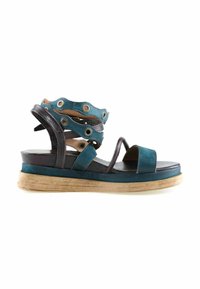 Sandale plate en cuir bleu sarcelle et noir avec bride à la cheville, ornée d'œillets métalliques et d'une semelle en bois.