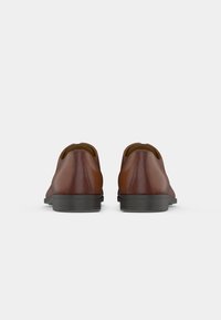 Brown leather shoes featuring a smooth finish, structured shape, and black rubber soles, shown from the back.