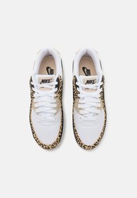 Bílé tenisky Nike s leopardím vzorem na bocích, mají černé akcenty, texturovaný síťovaný svršek a bílé tkaničky.