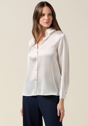 Light beige long-sleeve blouse in silky fabric, featuring a button-down front, classic collar, and cuff with gold-button detail.