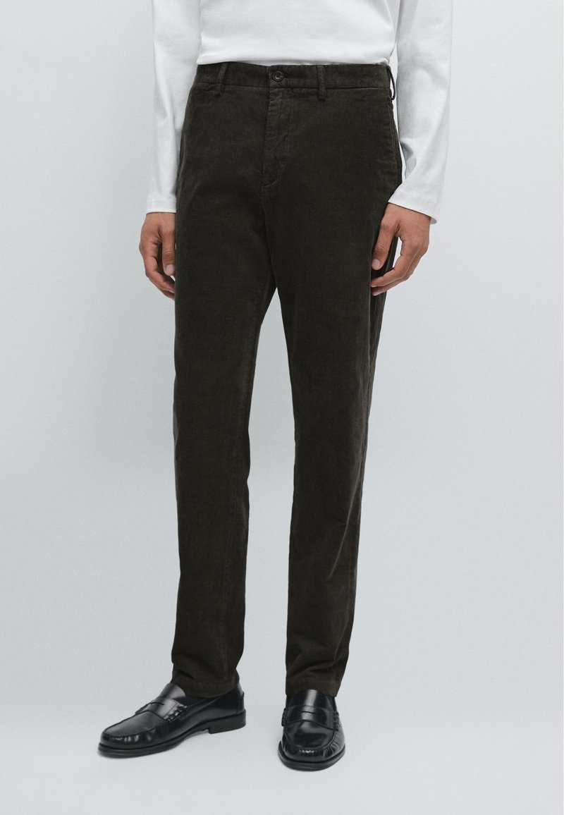 Pantaloni in corduroy marrone scuro con vestibilità dritta, tasche anteriori e chiusura a bottone, abbinati a mocassini in pelle nera.