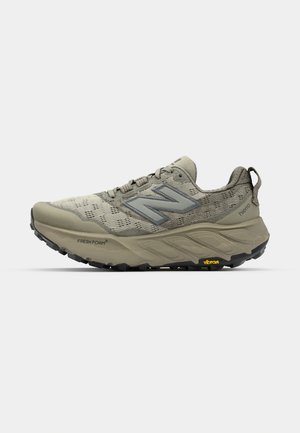 Lichtgrijze New Balance trailrunning schoenen met een bovenwerk van mesh, een gevoerde zool en een Vibram loopzool voor grip. Voorzien van reflecterende accenten.