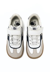 Zapatillas blancas y grises con una puntera de ante texturizado, acentos en azul marino, cierre con cordones y velcro, que presentan un gráfico de un oso en las plantillas.