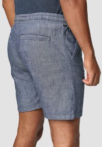 Shorts en lin bleu pour homme avec une taille à cordon, des poches latérales et une poche arrière. Le tissu a une finition texturée.