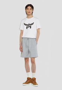 White cotton t-shirt with black graphic design, paired with gray drawstring shorts. Features tan high-top sneakers and white socks.