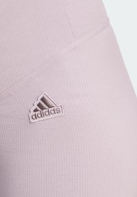 Nära bild av ljusrosa ribbade tygleggings med en liten broderad Adidas-logotyp på sidan.