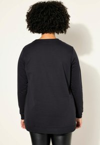 Felpa di un blu scuro navy con maniche lunghe, scollatura rotonda e una vestibilità ampia. Texture liscia, dettagli a coste sui polsini e sull'orlo ben visibili.