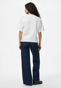 Bijela pamu�čna majica s kratkim rukavima, u kombinaciji s tamnoplavim širokim trapericama. Običan dizajn, bez vidljivih uzoraka ili akcenata.