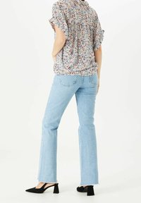 Blusa a fantasia floreale in tessuto leggero con maniche corte; abbinata a jeans a campana blu chiaro e scarpe con tacco nere.